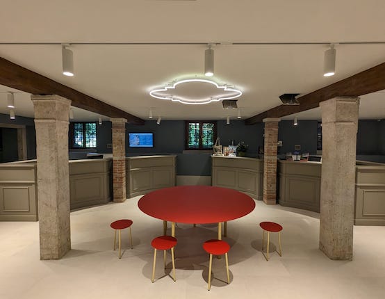 zona androne e infopoint ristrutturata con grosso tavolo rosso in mezzo